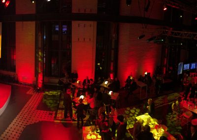 Sapophon Spieler und DJ auf Bühne, lange Tische davor, rote Beleuchtung im Saal