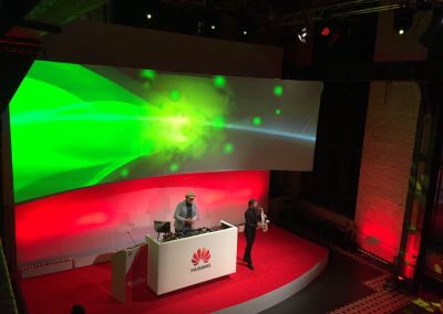 Bühne mit Saxophon Spieler, DJ, rotes Licht, Leinwand mit grünem Licht über Bühne