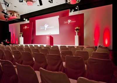 leere Stuhlreihen vor Bühne, rotes Licht, Mikrofone auf Bühne,