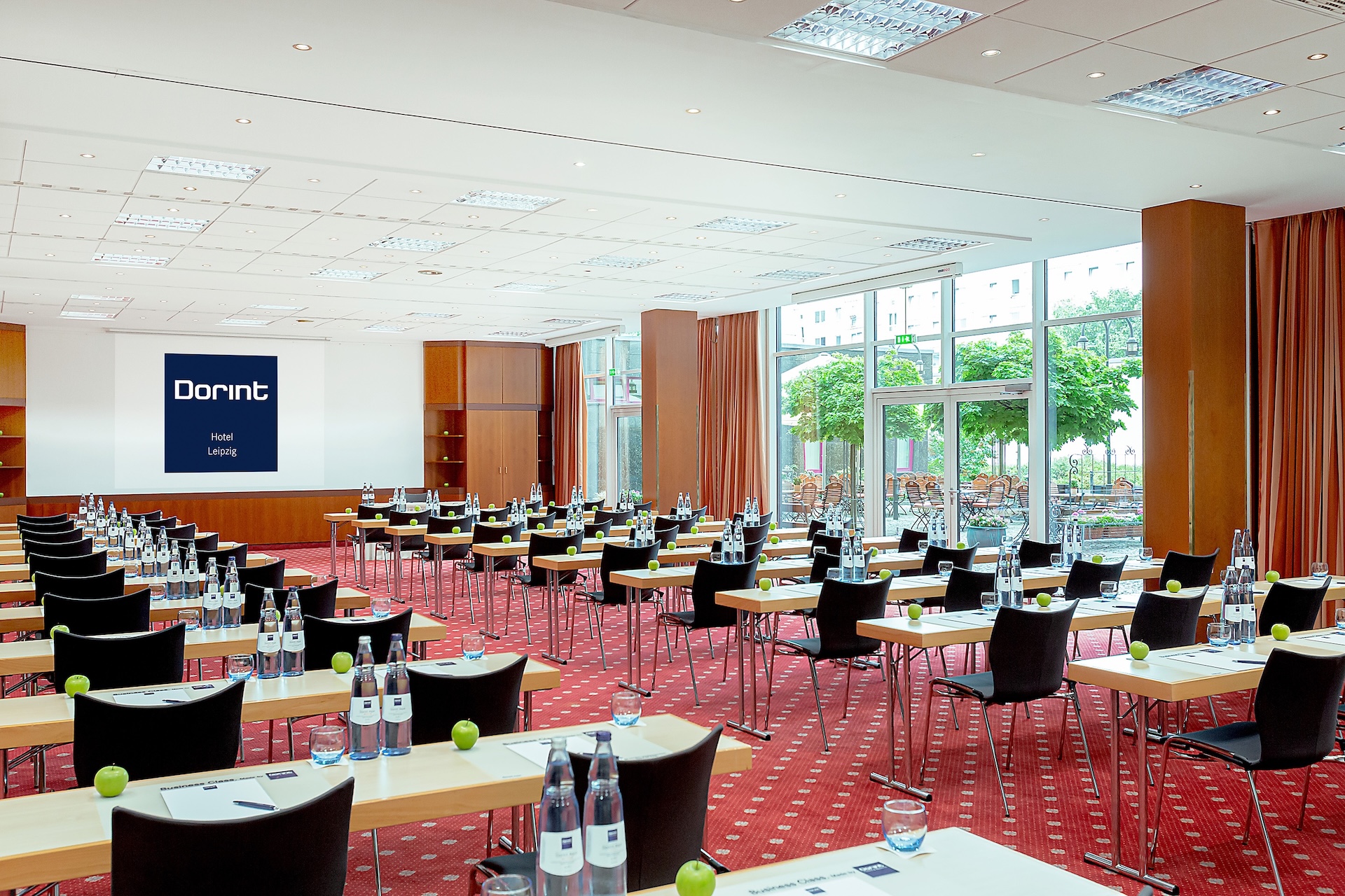 Heller Konferenzraum mit zur Leinwand und Konferenztechnik ausgerichteten Bestuhlung.
