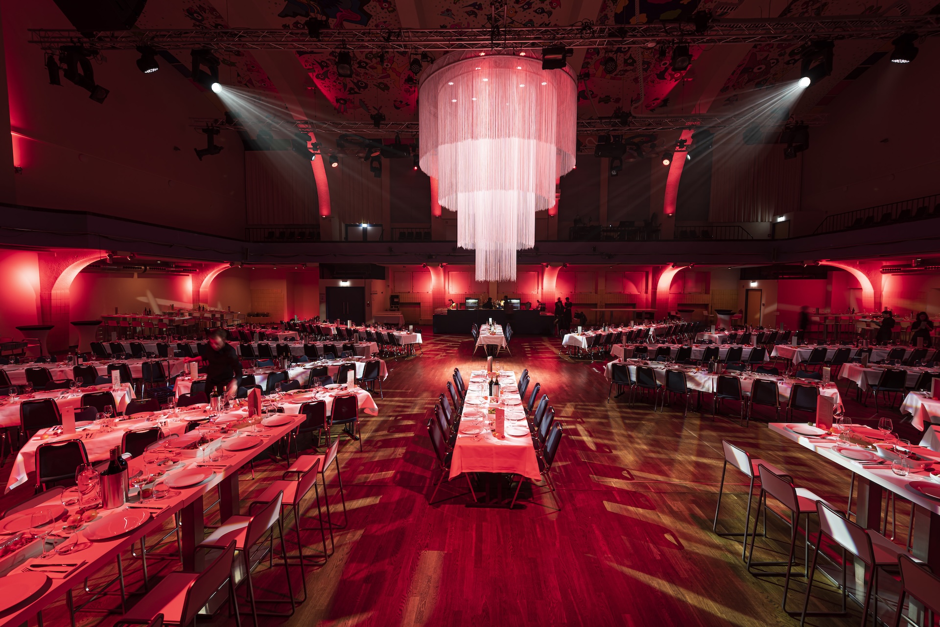 In rotes Ambientlicht getauchte Kuppelhalle bestuhlt und eingedeckt für ein Bankett.