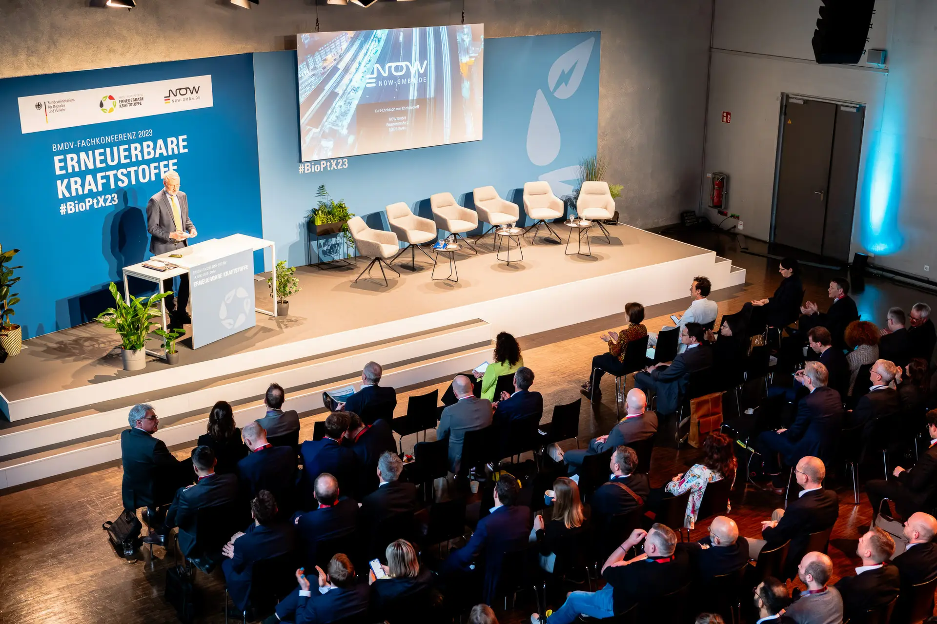 Hybrid Veranstaltung mit Bühne für live und zugeschaltete Vortragende und Reihenbestuhlung mit Publikum davor